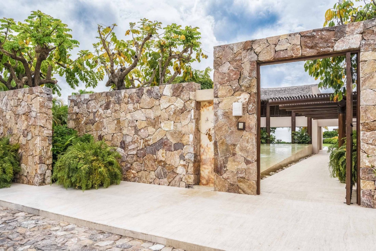 Contemporary stone entrance at Casa Caída de Agua surrounded by tropical landscaping and modern architecture